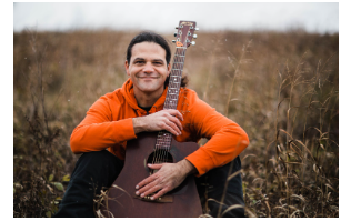Joe Reilly sitting in a field holding an acoustic guitar.